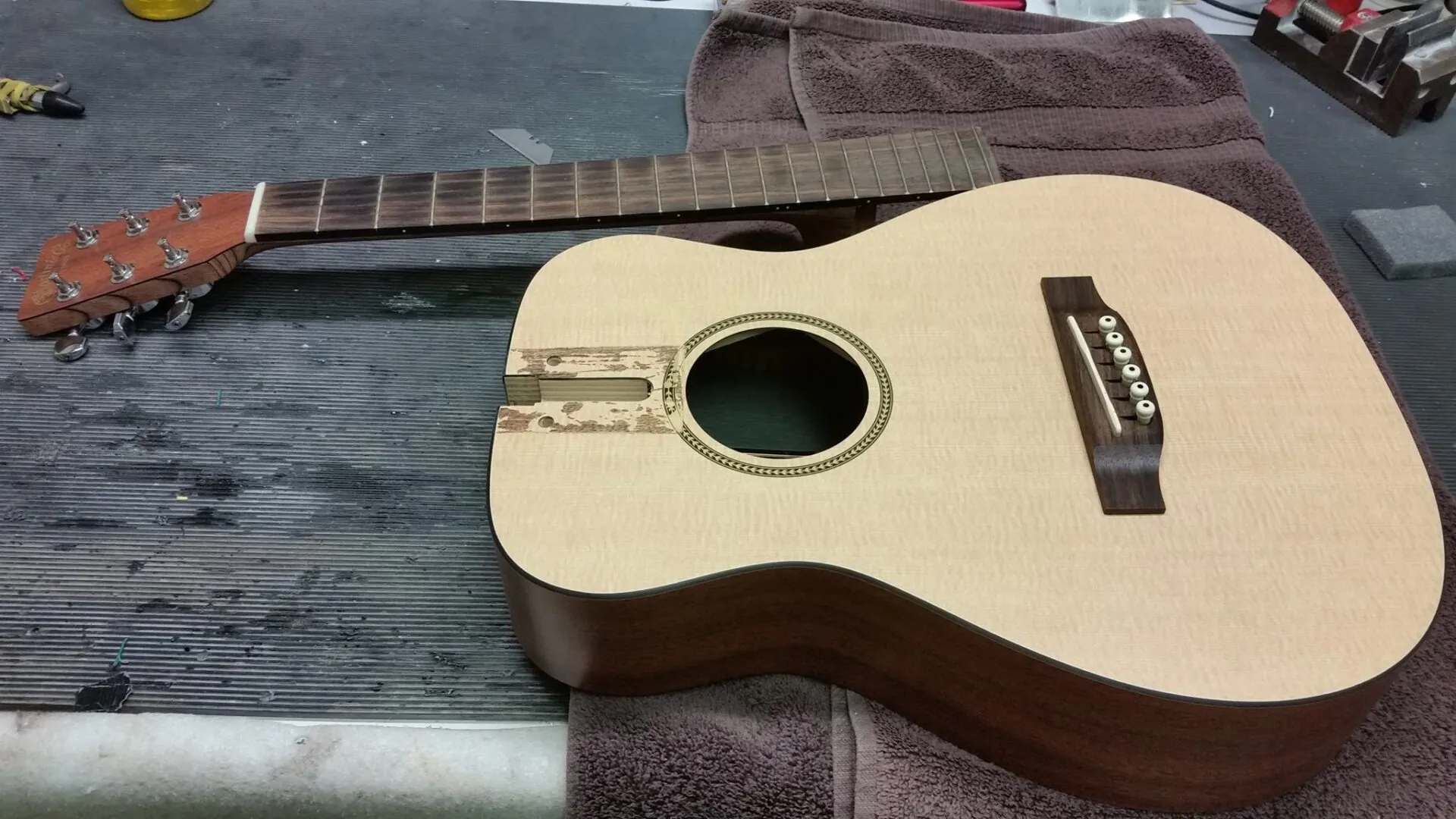 A small acoustic guitar with a spruce top lying on the padded workbench
