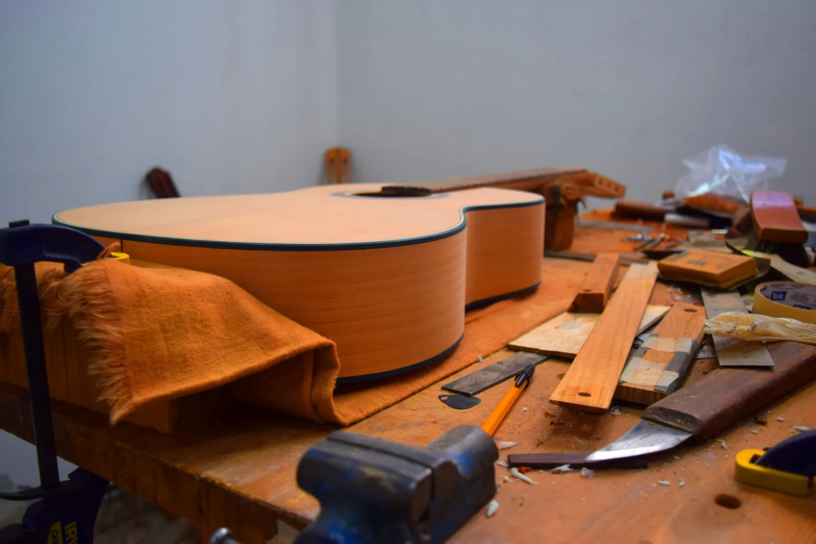 Unfinished acoustic guitar bodies on a workbench among clamps, wood strips and shavings