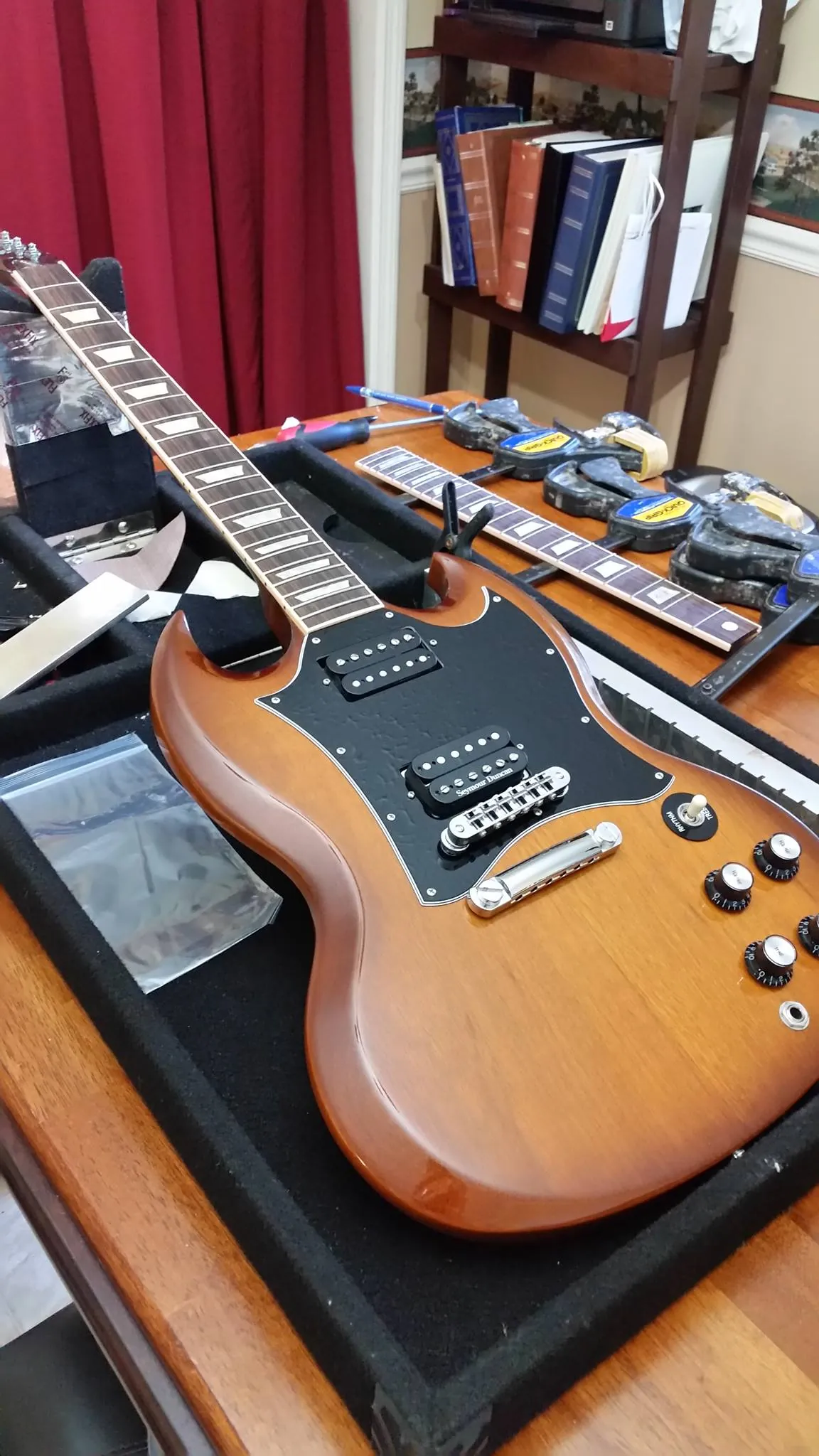 An SG-style guitar on the workbench beside spare fretboards and tools