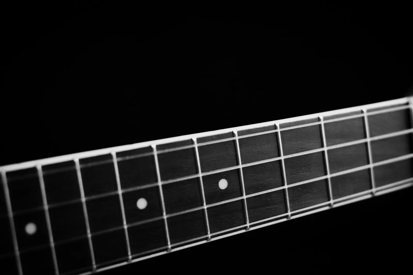 A dark fingerboard with dot inlays against a black background