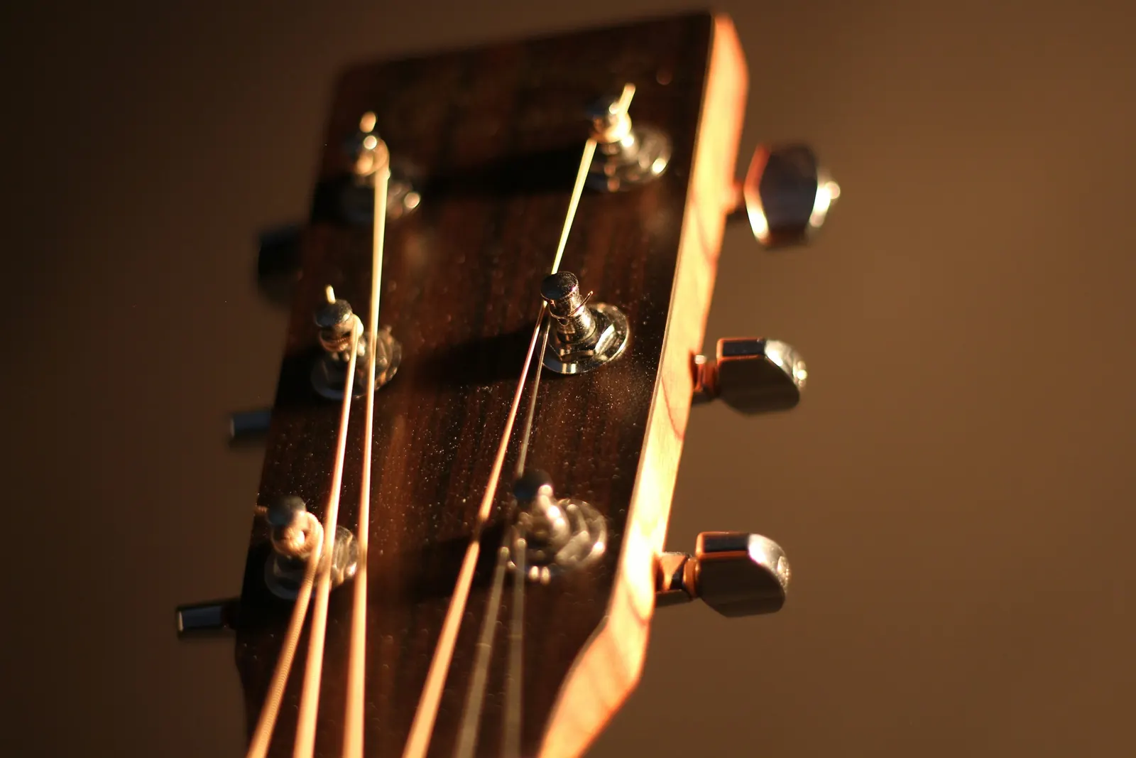 An acoustic guitar headstock with metal tuning pegs in warm light