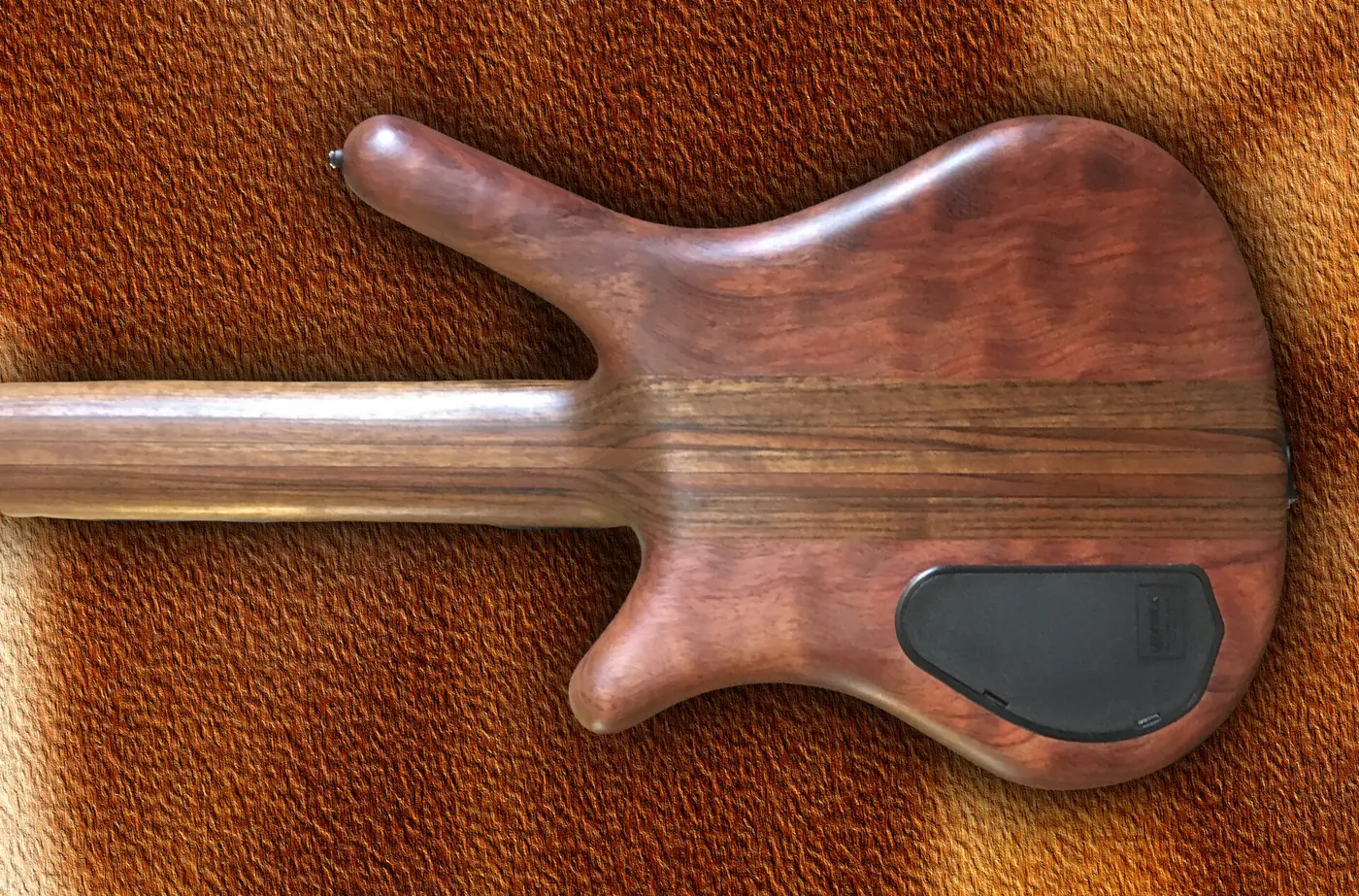 A dark figured wood bass body with three knobs, lying on brown leather