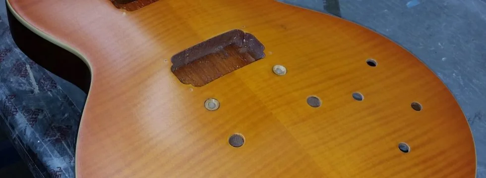 A sunburst flame maple guitar top with the pickups removed and the cavities showing