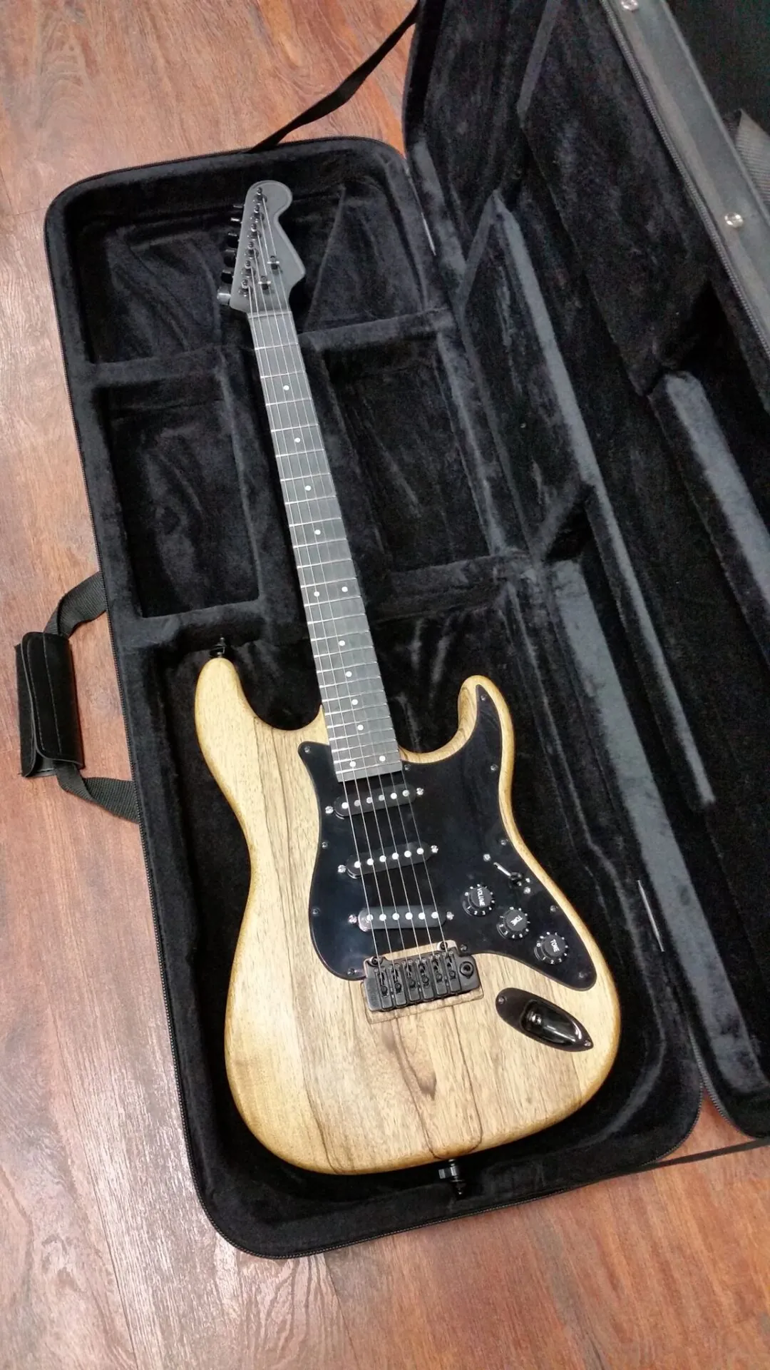 A natural ash Stratocaster-style guitar in an open case