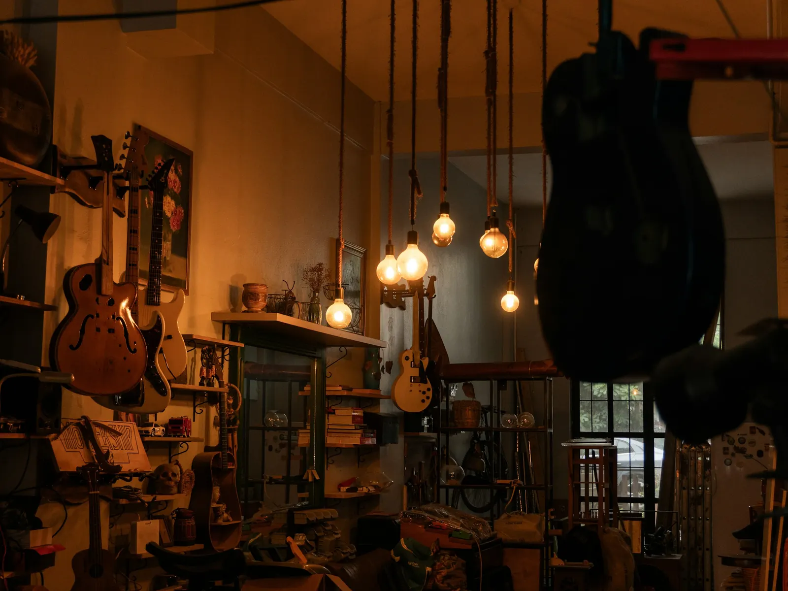 Guitars hanging in a dim workshop lit by bare bulbs