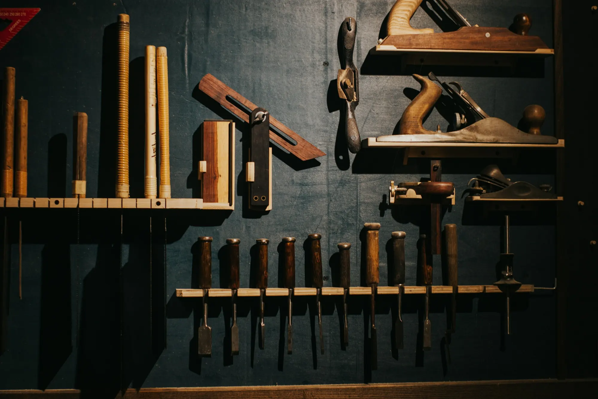 Hand planes, chisels and other woodworking tools on a dark workshop wall