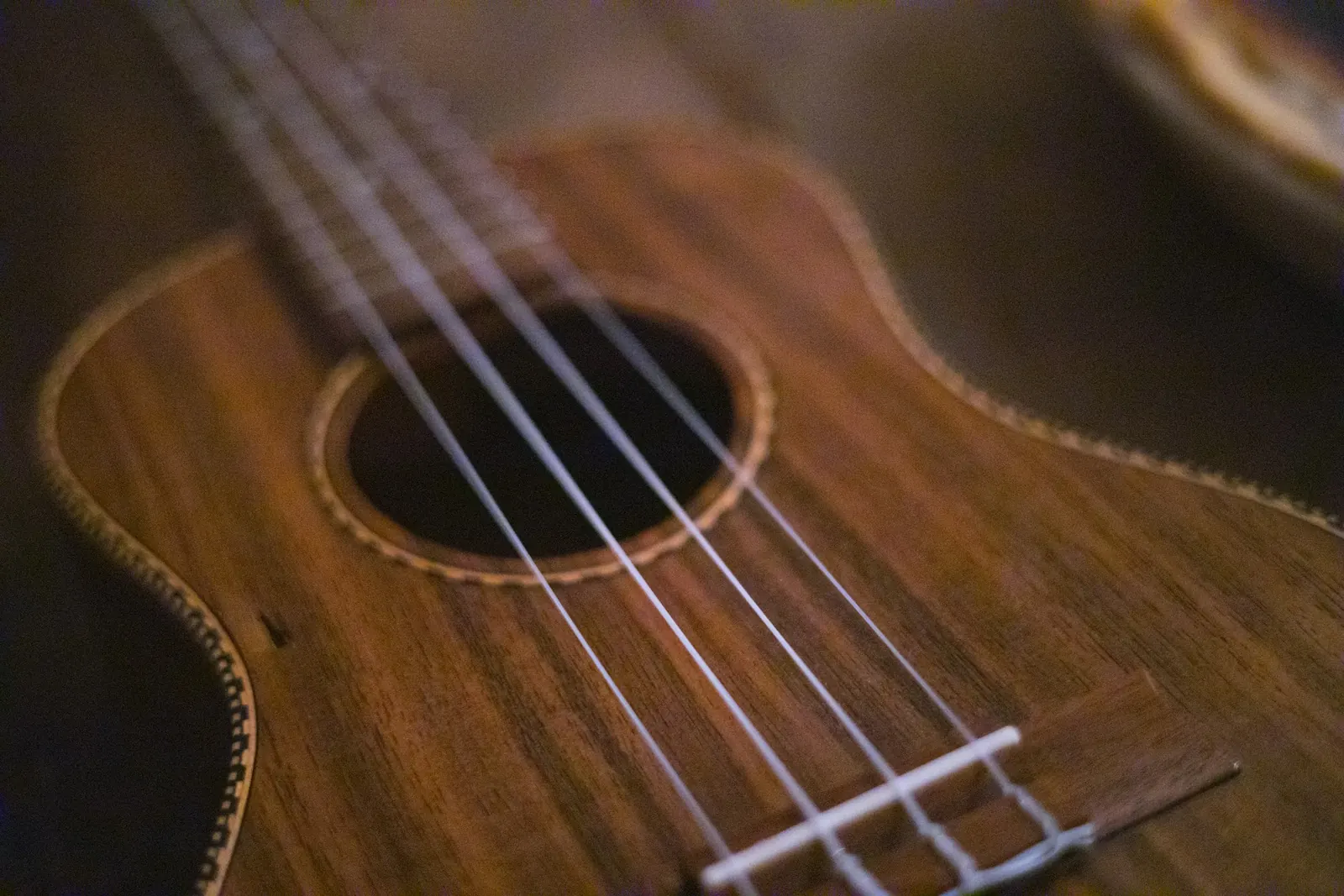 Strings over the soundhole of a koa ukulele in warm light