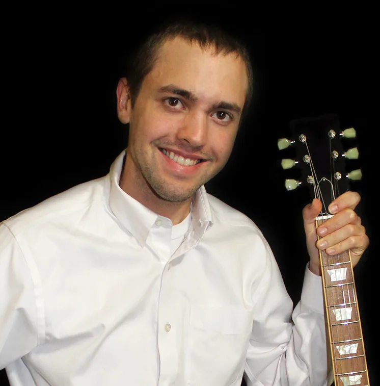 Wesley Wilkerson smiling, holding a guitar by the neck
